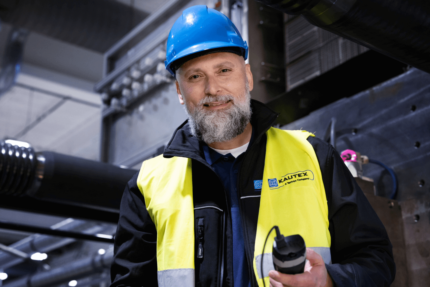 Man holding a walkie talkie wearing a hard hat and yellow vest