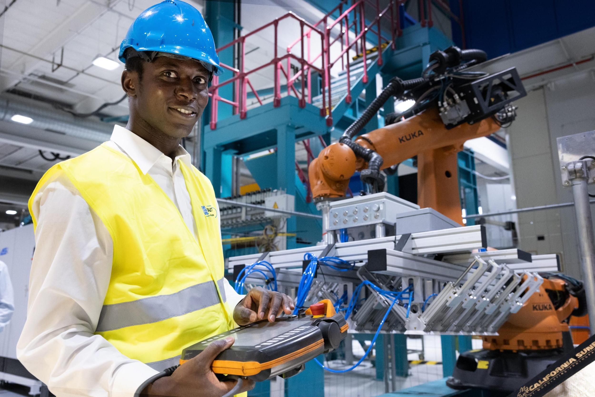 man standing in front of manufacturing plant, wearing a blue construction helmet and yellow vest