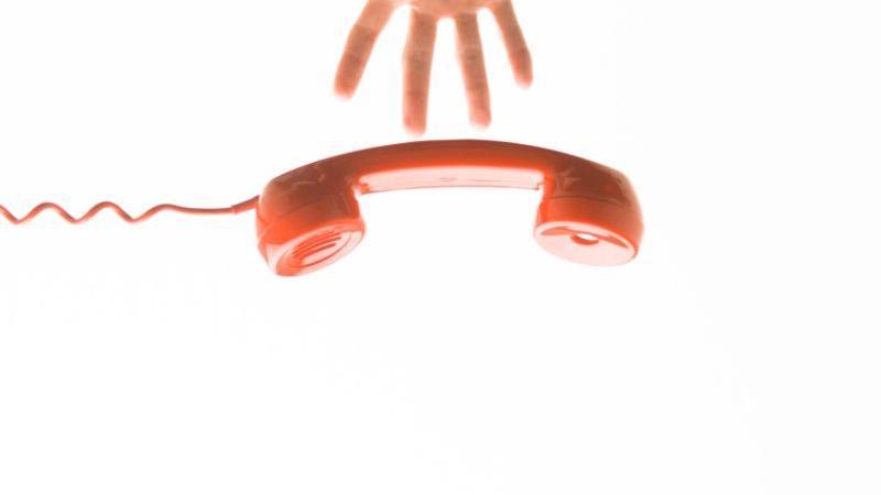 Red analog telephone being dropped, with a hand at the top of the image