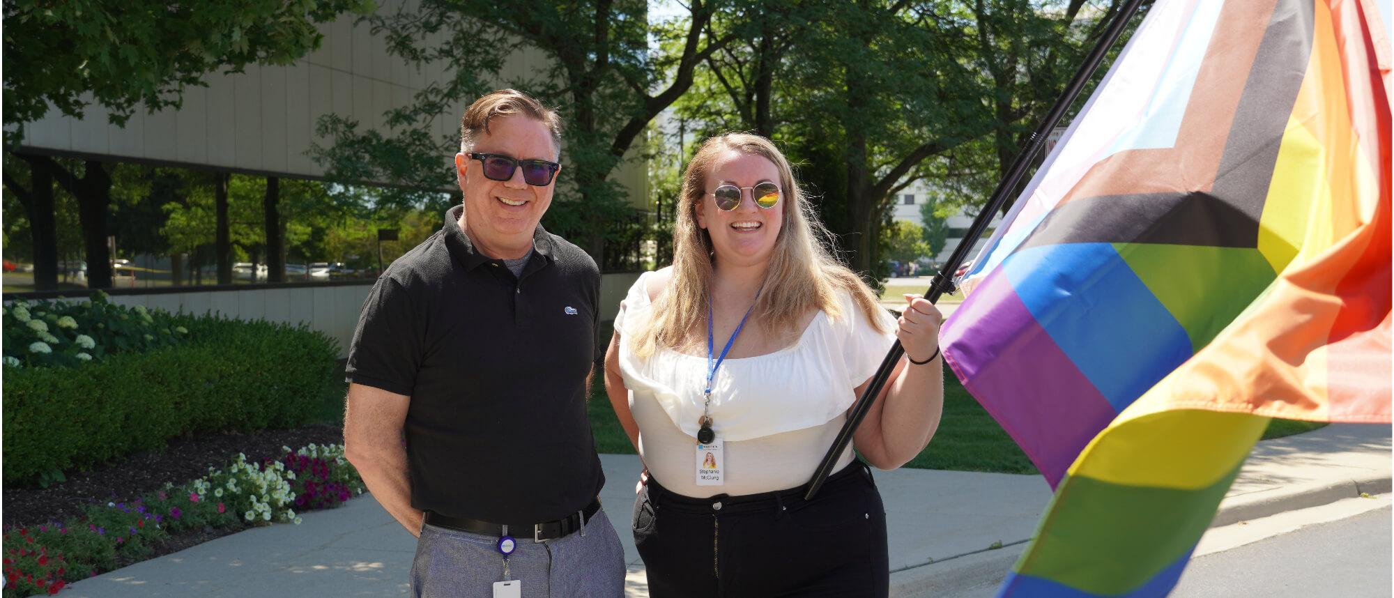 Two people standing outside holding a Pride flag